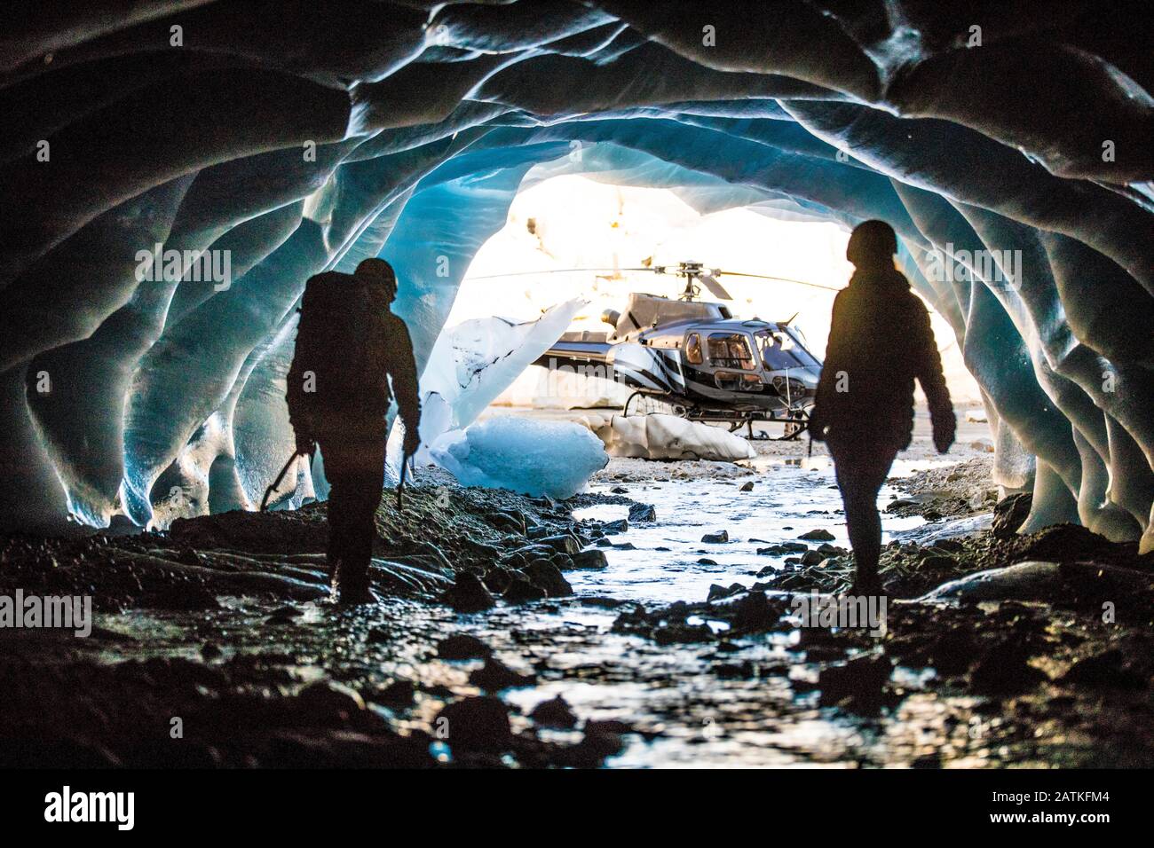Abenteuerlustige Paare tauchen aus einer Eishöhle auf, um ihren Hubschrauber zu finden. Stockfoto