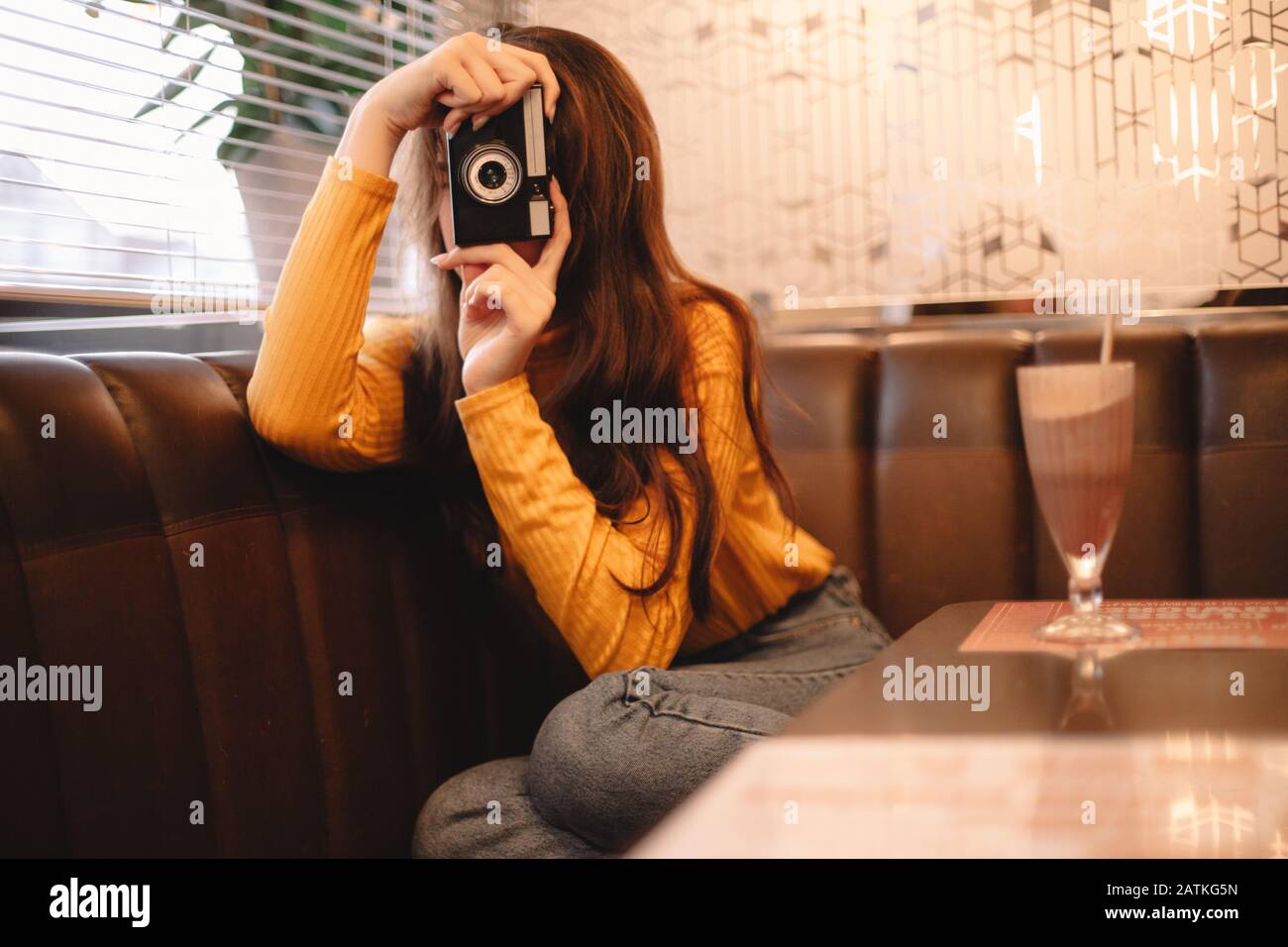 Junge Frau fotografiert mit Vintage-Kamera, während sie im Café sitzt Stockfoto