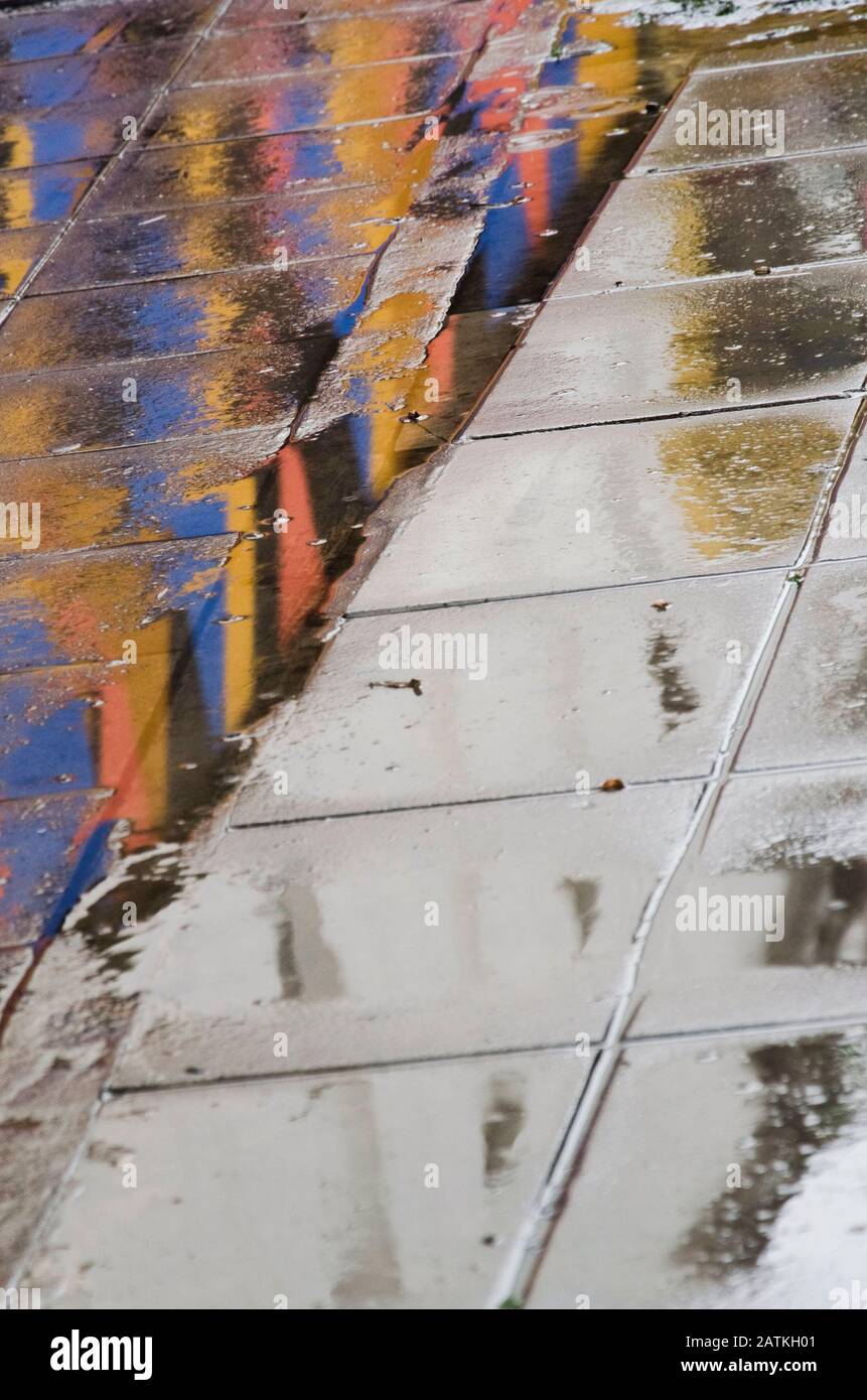 Urbaner Boden nach dem Regen spiegeln sich die Farben der Umgebung im nassen Boden wider und schaffen so ein interessantes Design Stockfoto