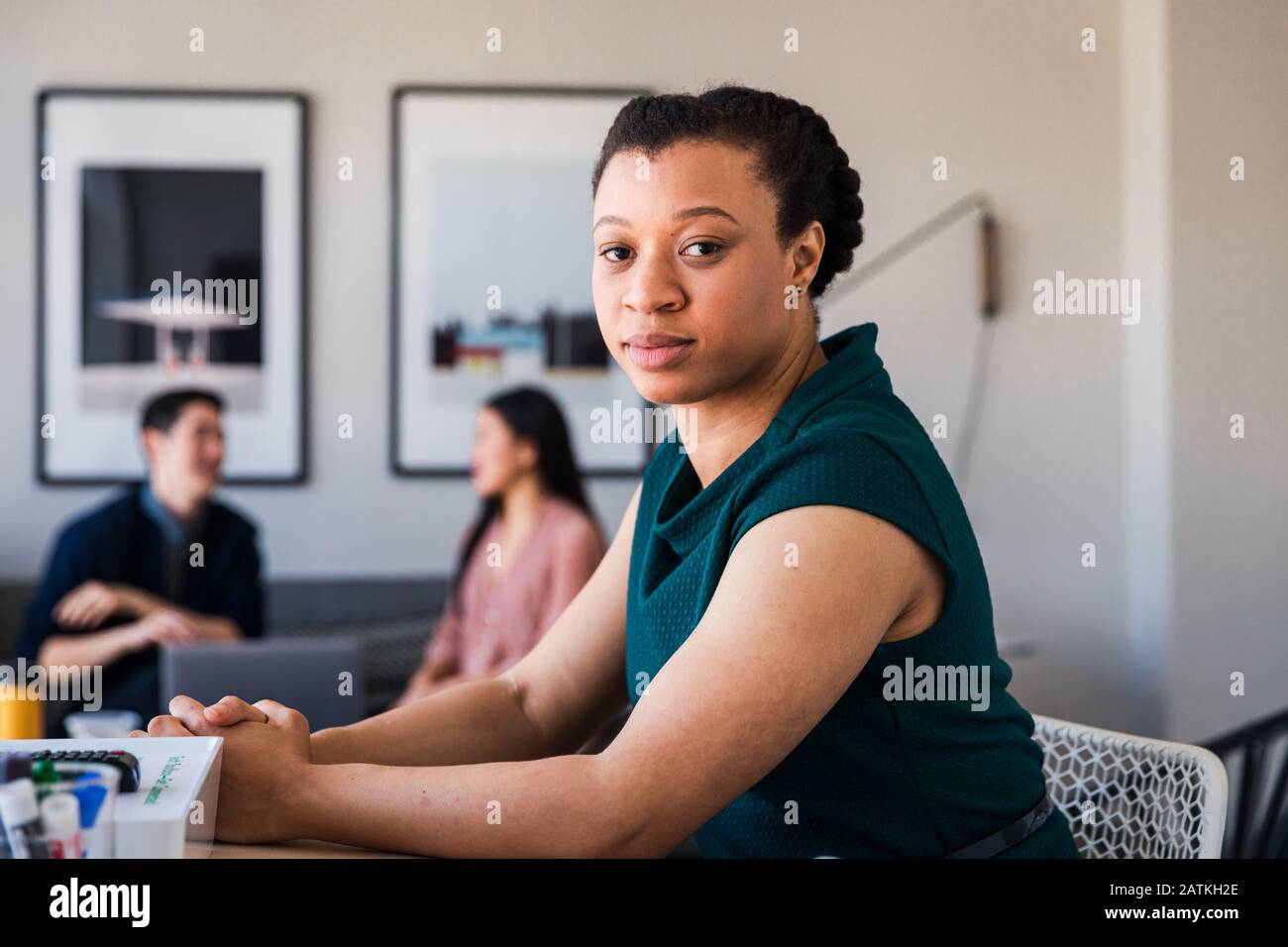Porträt einer selbstbewussten Geschäftsfrau, die mit Kollegen im Hintergrund am Tisch sitzt Stockfoto