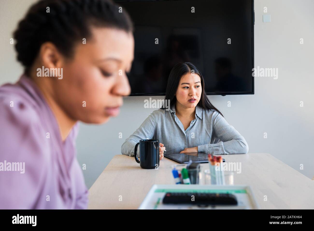 Durchdachte Geschäftsfrau, die Grafiktablett verwendet, während sie mit Kollegen im Büro sitzt Stockfoto