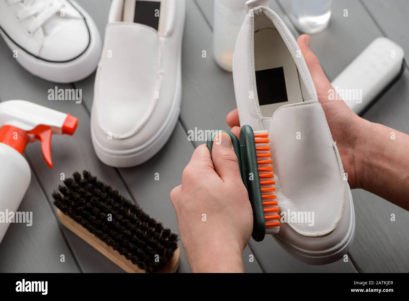 Weiße Lederschuhe reinigen. Mann mit Bürsten und Waschmittelschaum Stockfoto