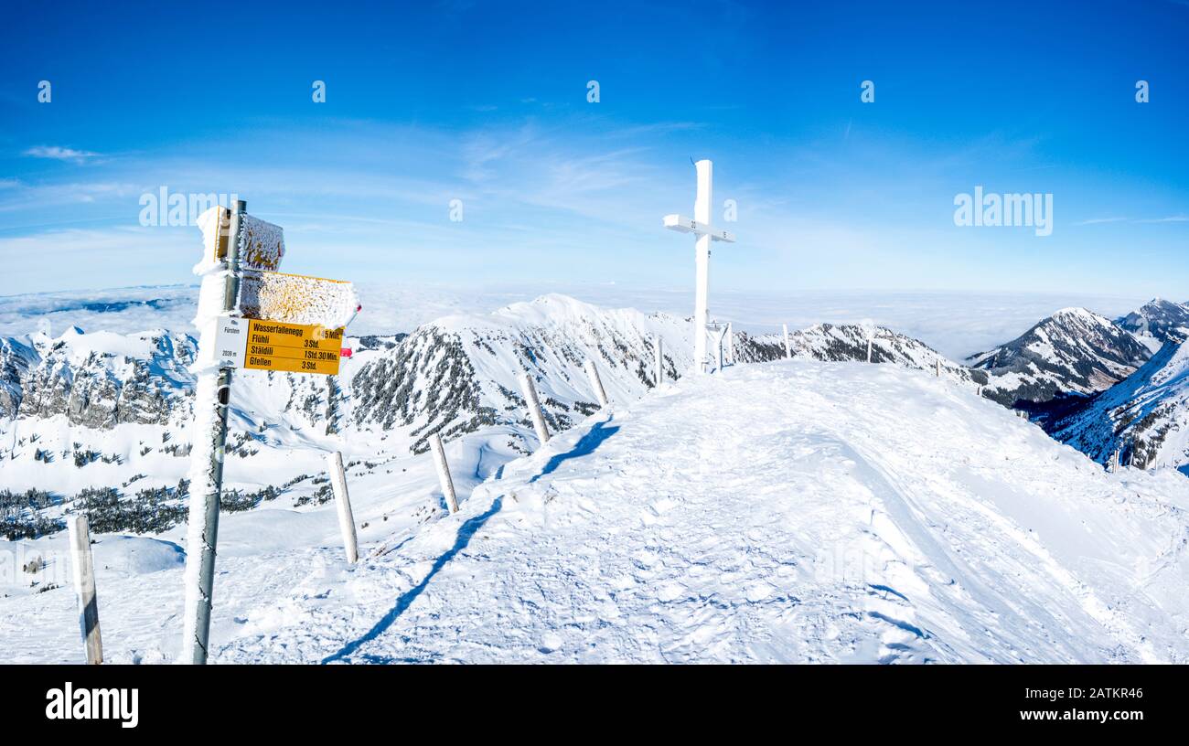 Gefrorener Wegweiser und Kreuz auf dem Gipfel des verschneiten Gebirges. Herrliches Bergpanorama in der schweiz auf fuerstein, schweizer alpen Stockfoto