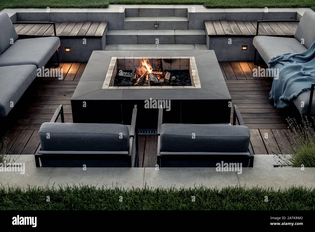 Relax Zone mit Holzboden und einem gefliesten Treppe im Freien. Es ist eine brennende Feuergrube, grauen Sofas und Sesseln, Plaid, leuchtende Lampen. Horizontale. Stockfoto