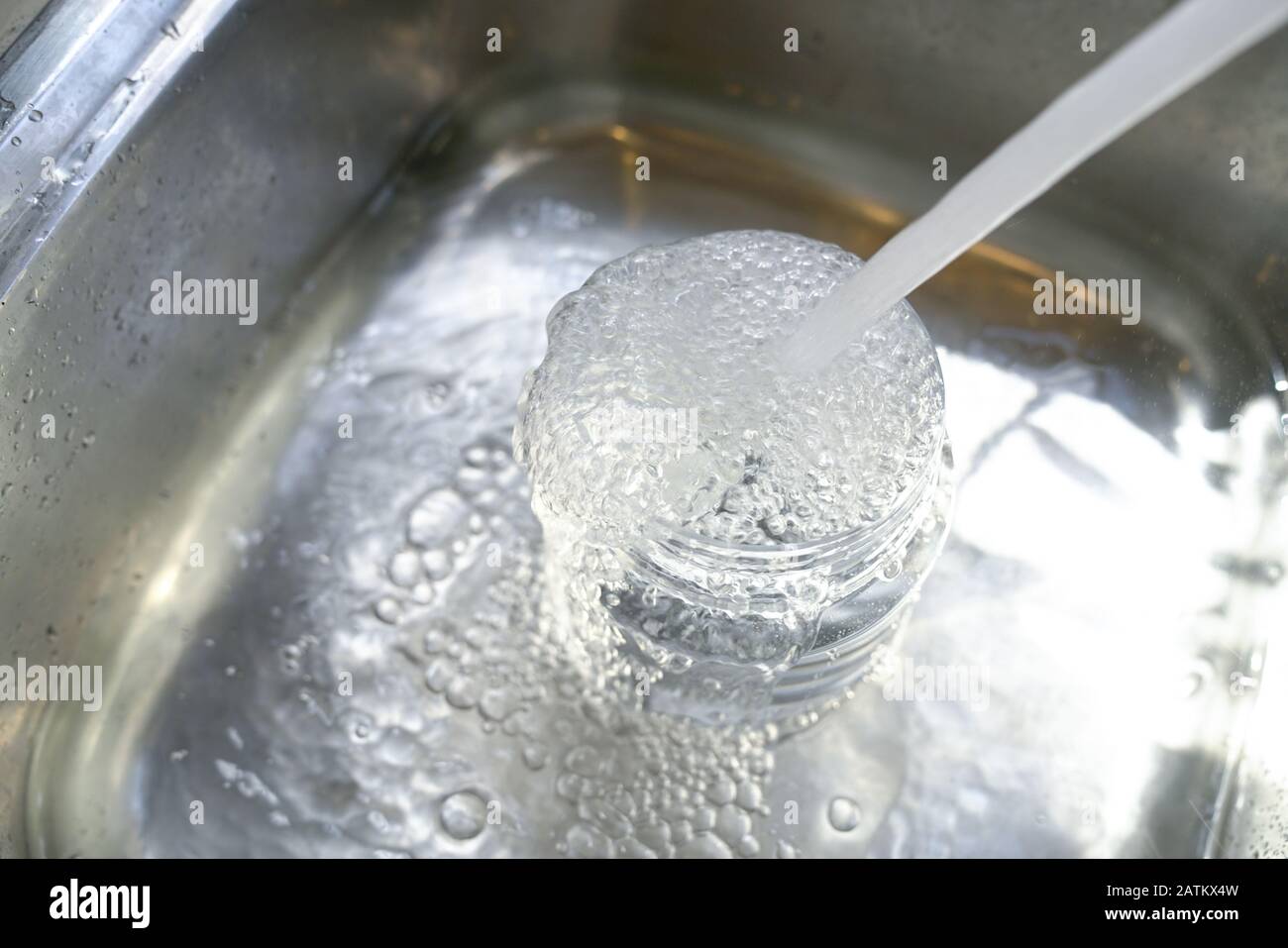 Wasser aus dem Hahn in den Kunststoffbehälter und es läuft zum Waschbecken über. Wasserkonzept sparen. Stockfoto