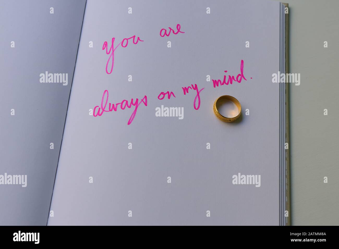 Goldener Ring auf Notizbuch mit Handschrift in pinkfarbener Farbe Lesen Sie sind immer auf meinem Kopf, das Buch ist auf weißem Holztisch, Liebeskonzept Stockfoto