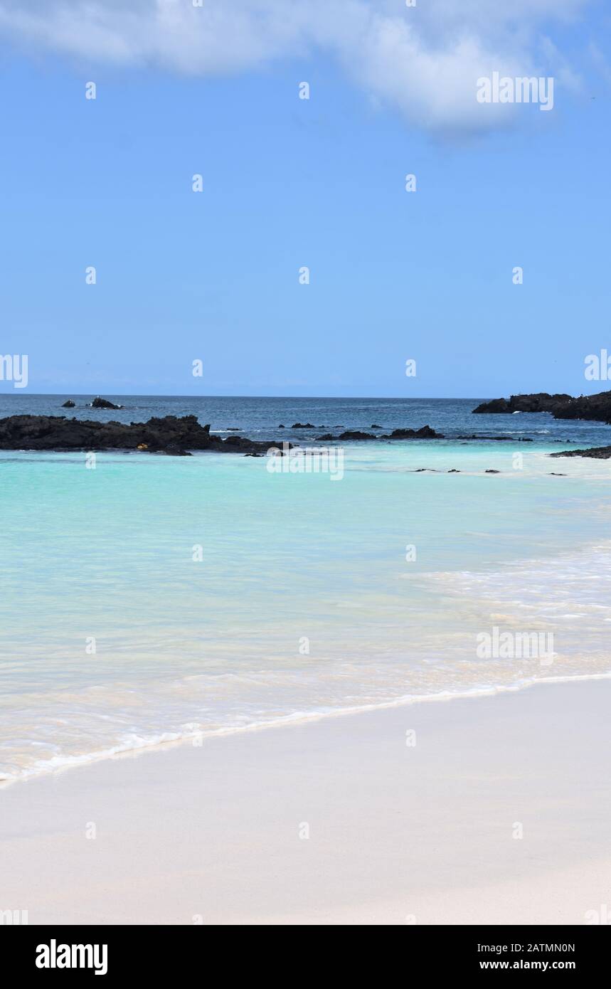 Sandiger tropischer Strand und blaues türkisfarbenes Meerwasser unter blauem Himmel und Lavasteinen Stockfoto