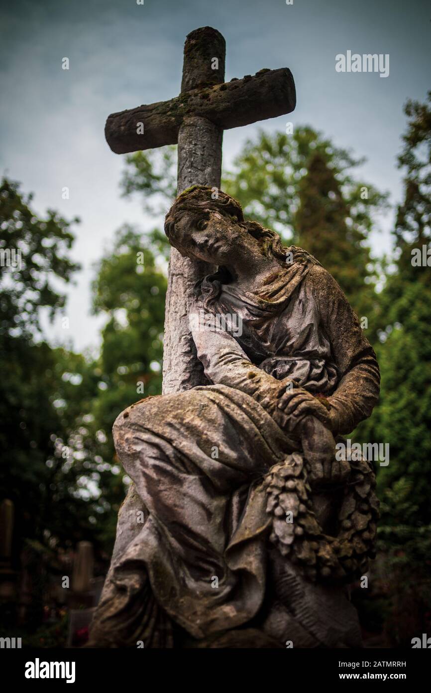 Alte Steinskulptur der kontemplativen Frau, die sich auf dem historischen Rakowicki-Friedhof in Krakow, Polen, am Kreuz auflehnt Stockfoto