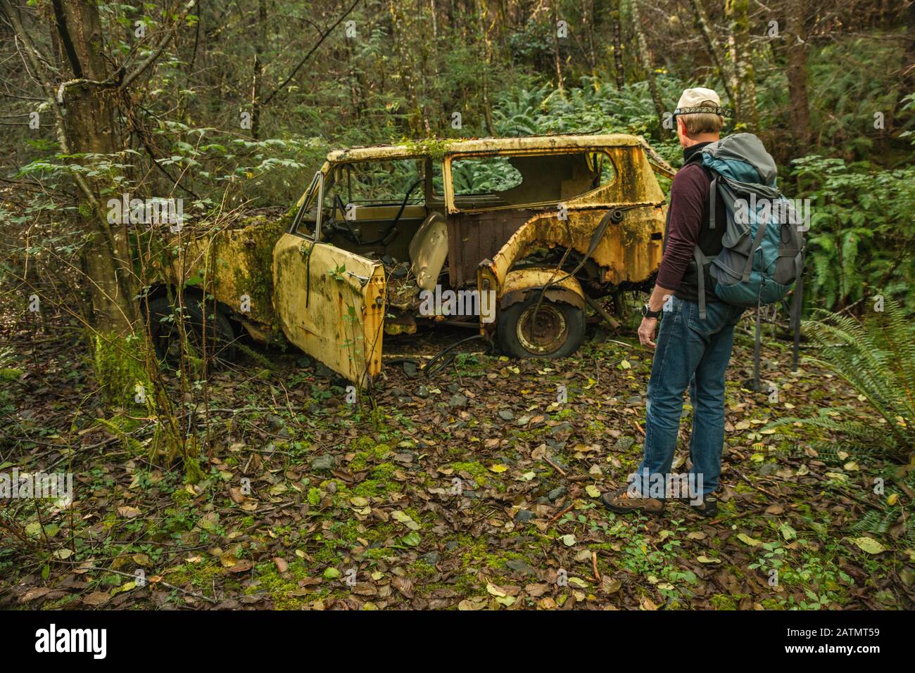 Wanderer auf Maude alias Maud Island Trail, mit Blick auf das alte, verlassene Geländefahrzeug im Regenwald, Quadra Island, British Columbia, Kanada Stockfoto