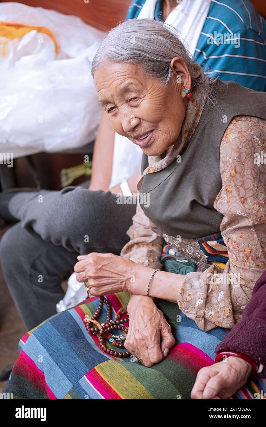 Eine ältere buddhistische Frau, die eine Chupa trägt und Gebetsperlen hält. Bei einem Musikkonzert in einem Tempelkeller in Elmhurst, Queens, New York. Stockfoto