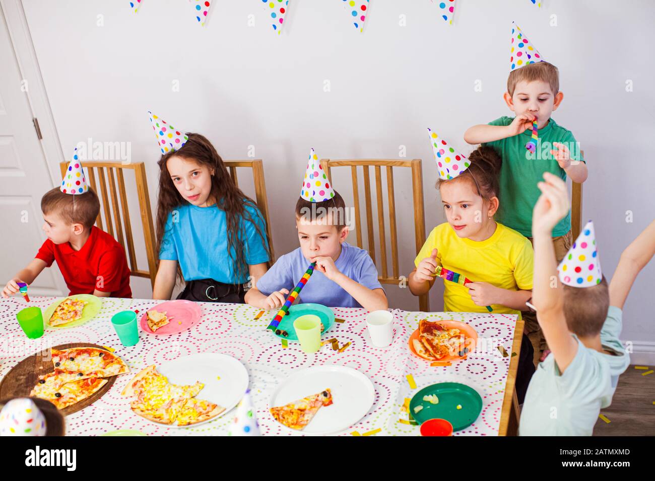 Kinder feiern Geburtstag mit einer Pizza im Café. Geburtstagsfeier. Süße Kinder in Geburtstagshüten, die zusammen Spaß haben Stockfoto