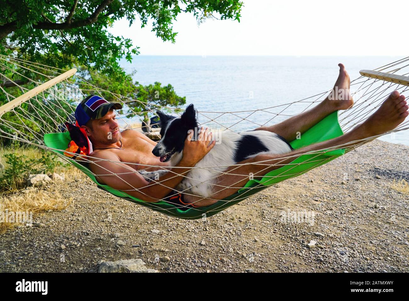 Ein junger Mann ruht mit einem Hund in einer Hängematte am Strand Stockfoto