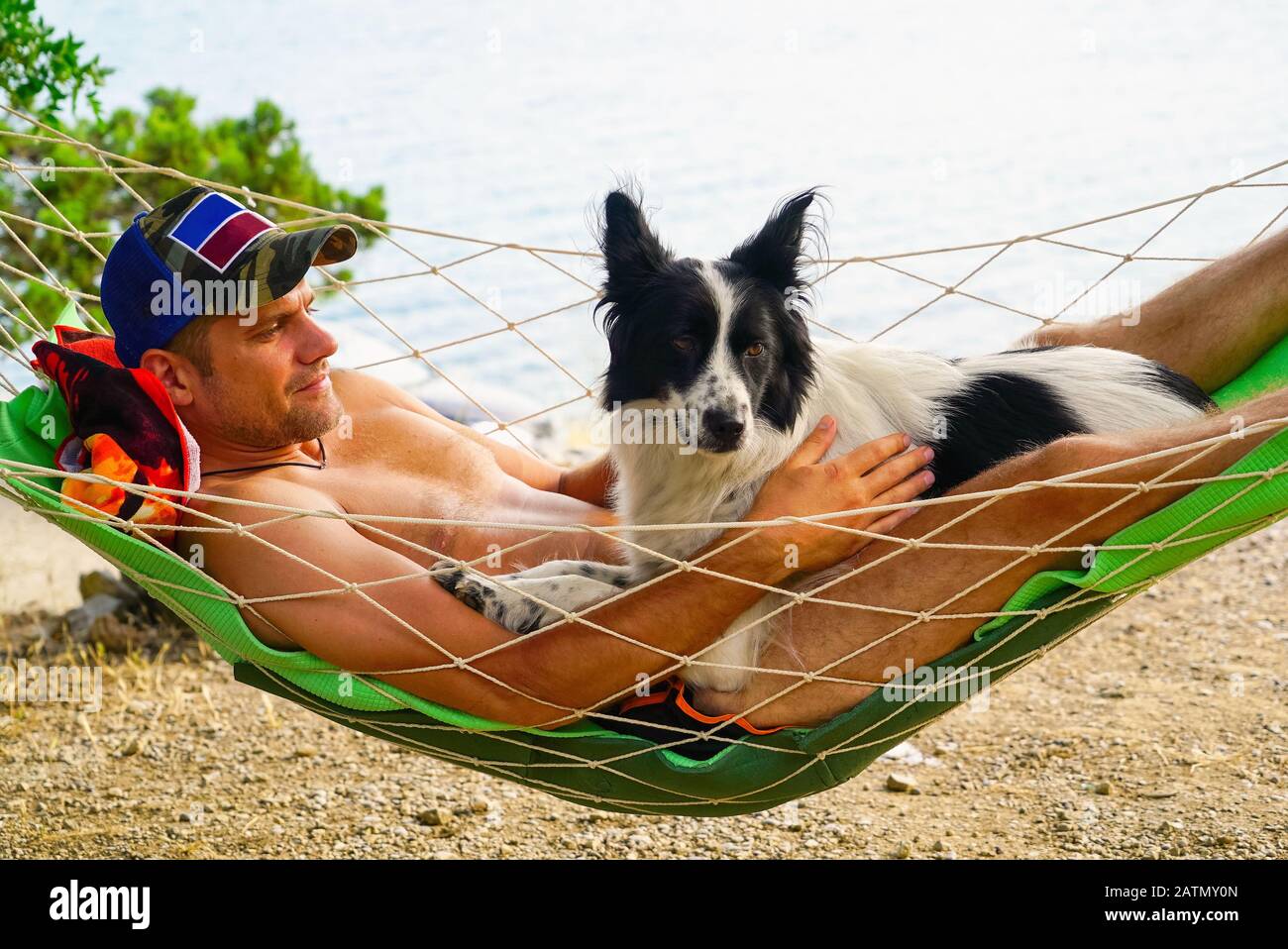 Ein junger Mann ruht mit einem Hund in einer Hängematte am Strand Stockfoto
