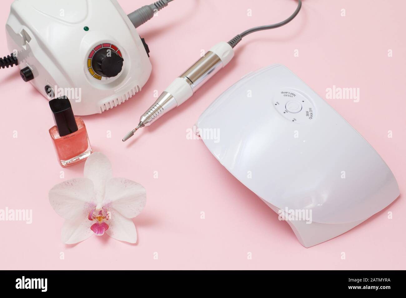 Fräser, LED-UV-Lampe, nagelpole und Orchideenblume auf pinkfarbenem Hintergrund. Eine Reihe von kosmetischen Tools für professionelle Hardwaremaniküre. Draufsicht. Stockfoto
