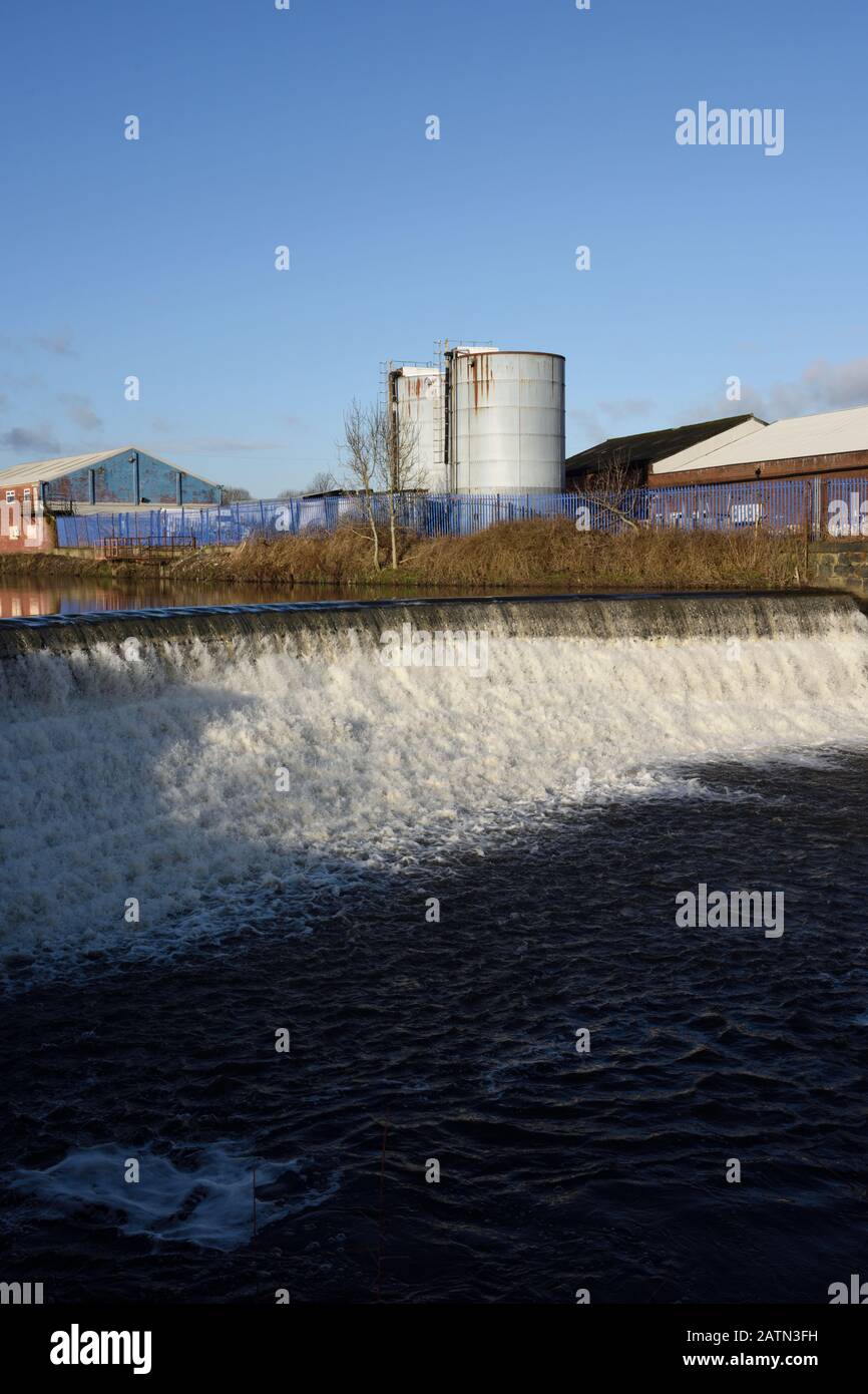 Weir am Fluss irwell mit Industriegebäuden und Silos im Hintergrund in radcliffe, Bury lancashire UK Stockfoto