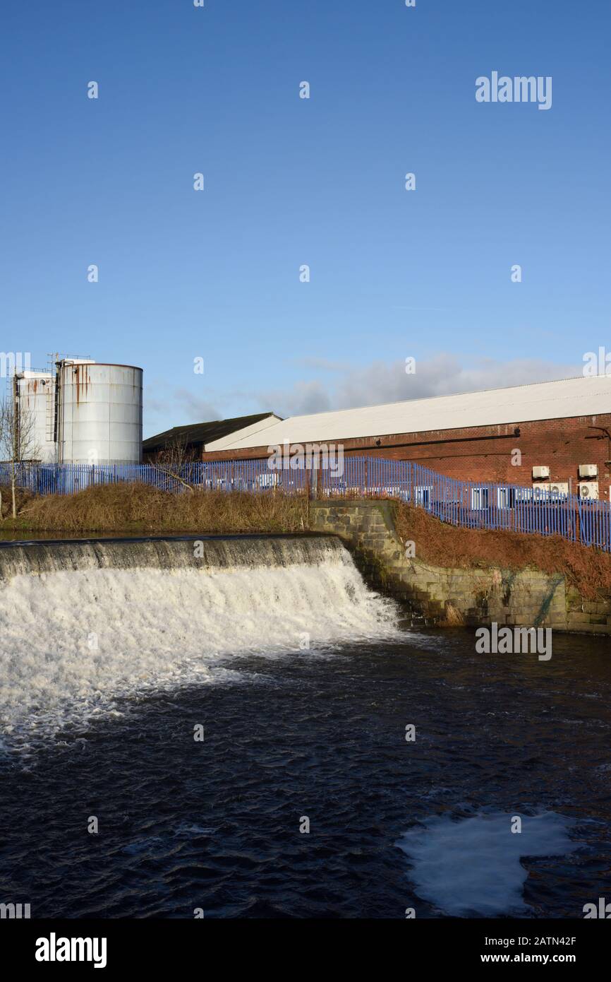 Weir am Fluss irwell mit Industriegebäuden und Silos im Hintergrund in radcliffe, Bury lancashire UK Stockfoto