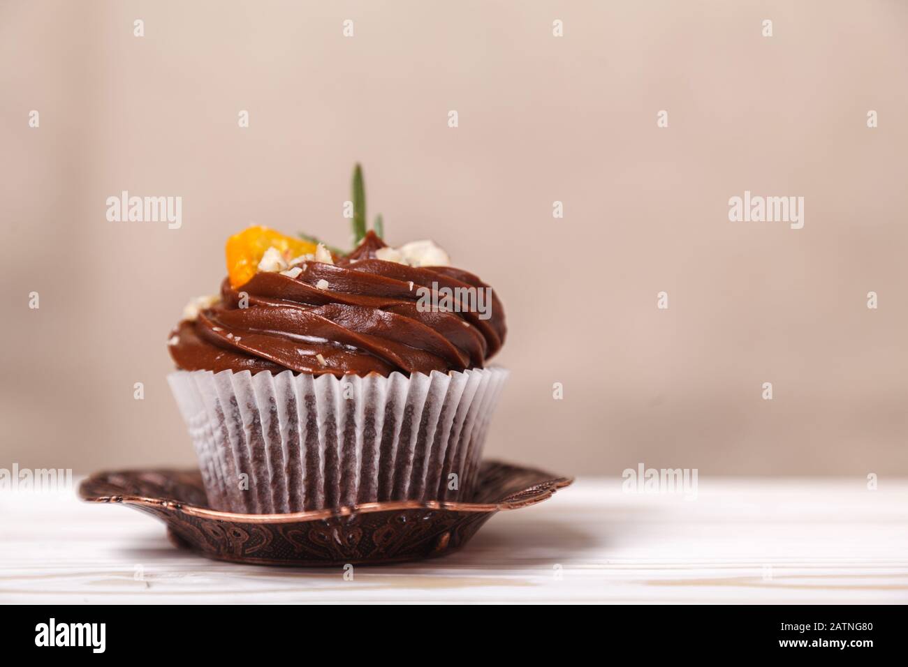 Köstlicher Cupcake mit Schlagsahne und Schokolade auf einem verschwommenen Hintergrund aus beigefarbener Wand. Konzept der Werbung für Süßwaren Stockfoto