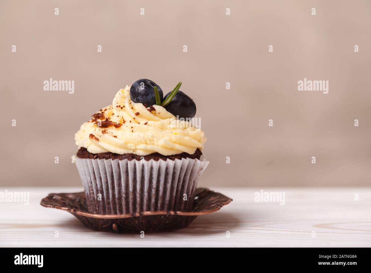 Köstlicher Cupcake mit Schlagsahne und Schokolade auf einem verschwommenen Hintergrund aus beigefarbener Wand. Konzept der Werbung für Süßwaren Stockfoto