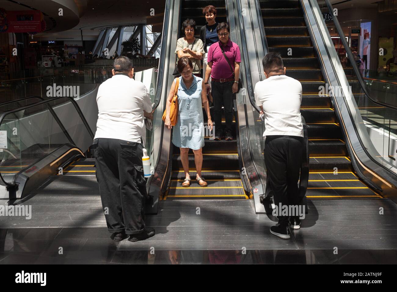 31.01.2020, Singapur, Republik Singapur, Asien - Menschen fahren auf einer Rolltreppe innerhalb des neuen Jewel-Terminals am Flughafen Changi, da zwei Arbeiter sauber sind. Stockfoto