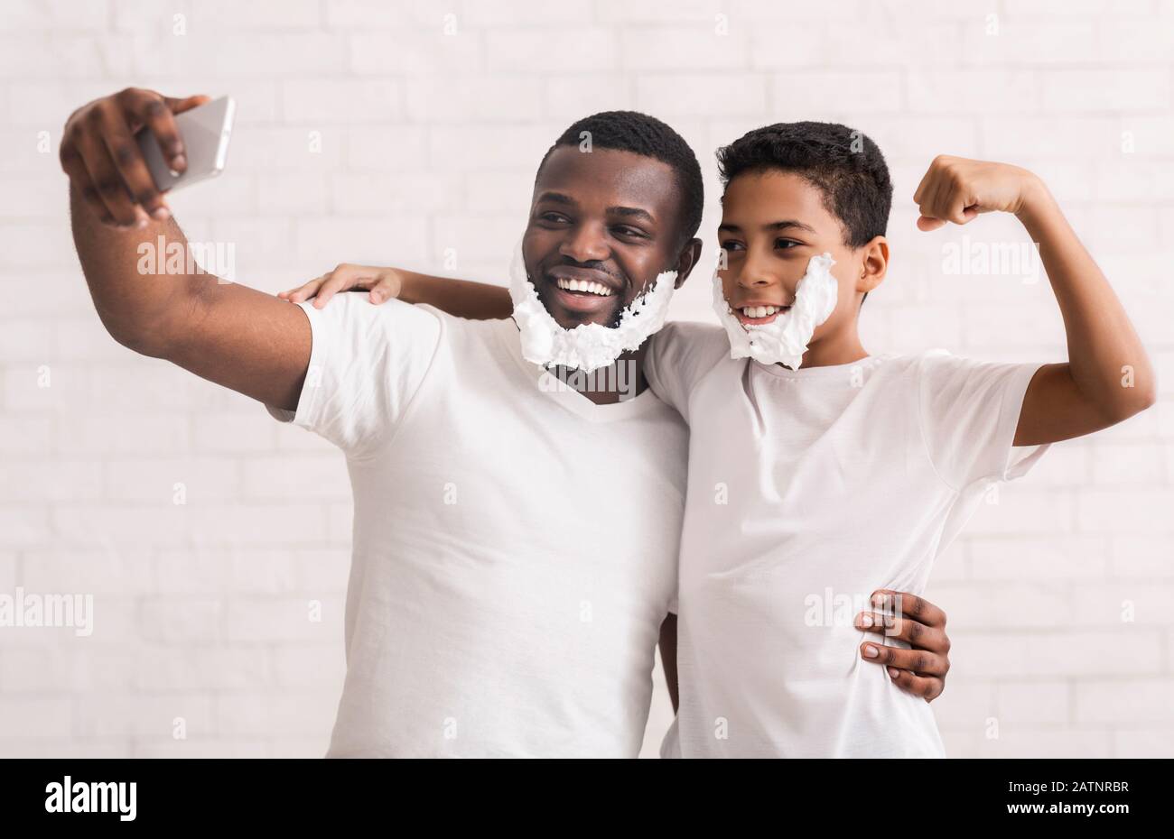 Männliche selfie. Vater und Sohn gemeinsam Spaß haben, mit Rasierschaum auf Handy Kamera posieren, grau studio Hintergrund Stockfoto