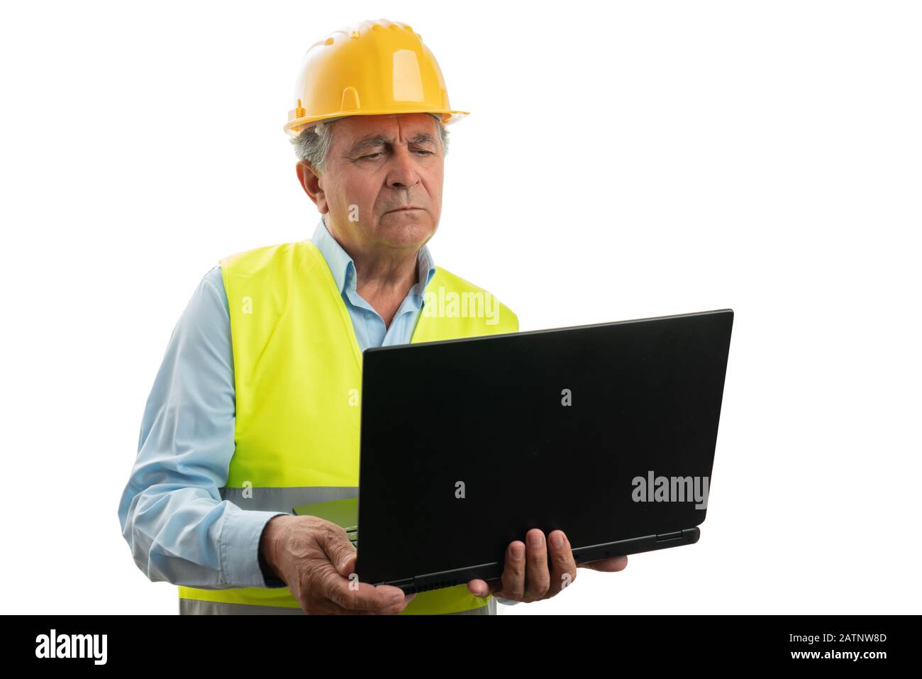 Der seriöse alte Architekt, der Weste und Hardhut trägt und auf einem weißen Studiohintergrund auf einen Laptop blickt Stockfoto