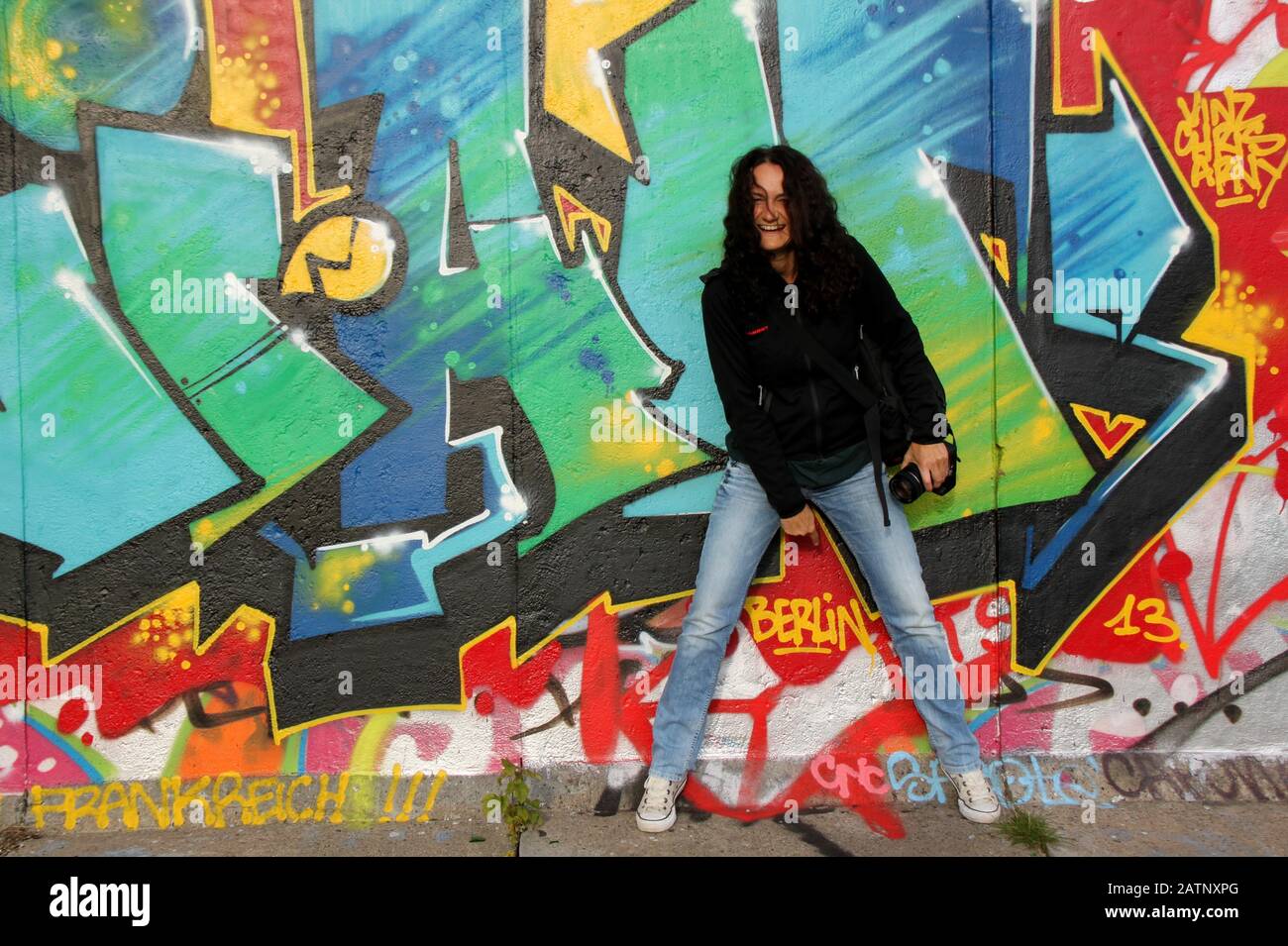 Frau, die vor der Berliner Mauer mit bunten Graffiti steht Stockfoto