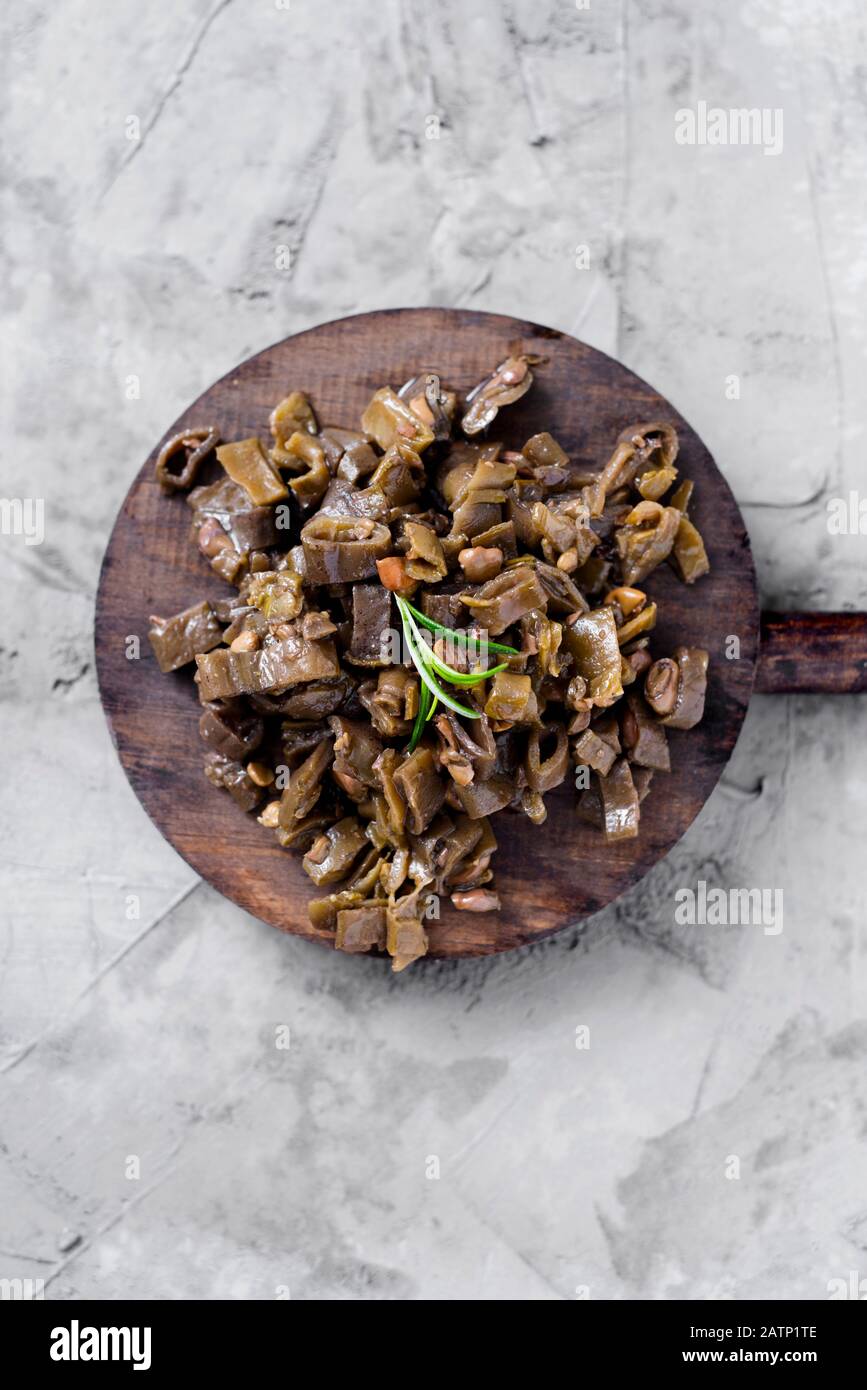 Hochwinkeliger Blick auf ein Holztablett mit Hhabas fritas, einem spanischen Rezept für breite Bohnen in seinen für Andalusien typischen Schoten, auf einer grauen rustikalen Betonsurfa Stockfoto