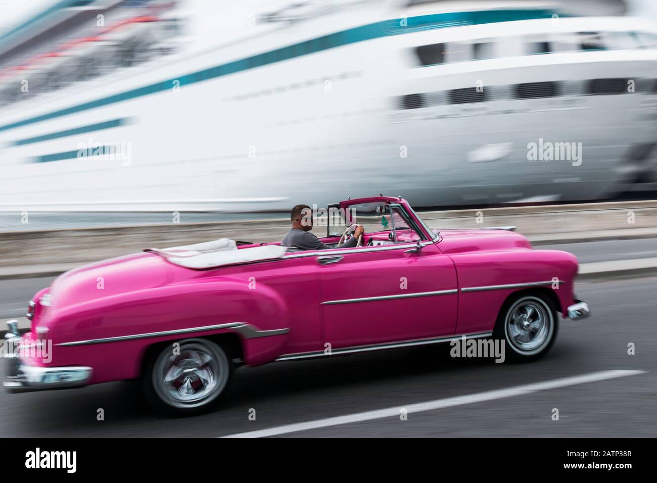 Havanna, Kuba - 25. Juli 2018: Rosafarbenes Cabriolet-Taxi der 1950er Jahre, das von einem Kreuzfahrtschiff mit verschwommenem Hintergrund zum Kreuzfahrtterminal in Havanna gefahren wird Stockfoto