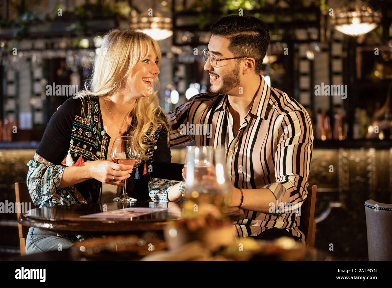 Ein heterosexuelles Paar sitzt und trinkt zusammen in einer Bar, während es sich betrachtet und lächelt. Stockfoto