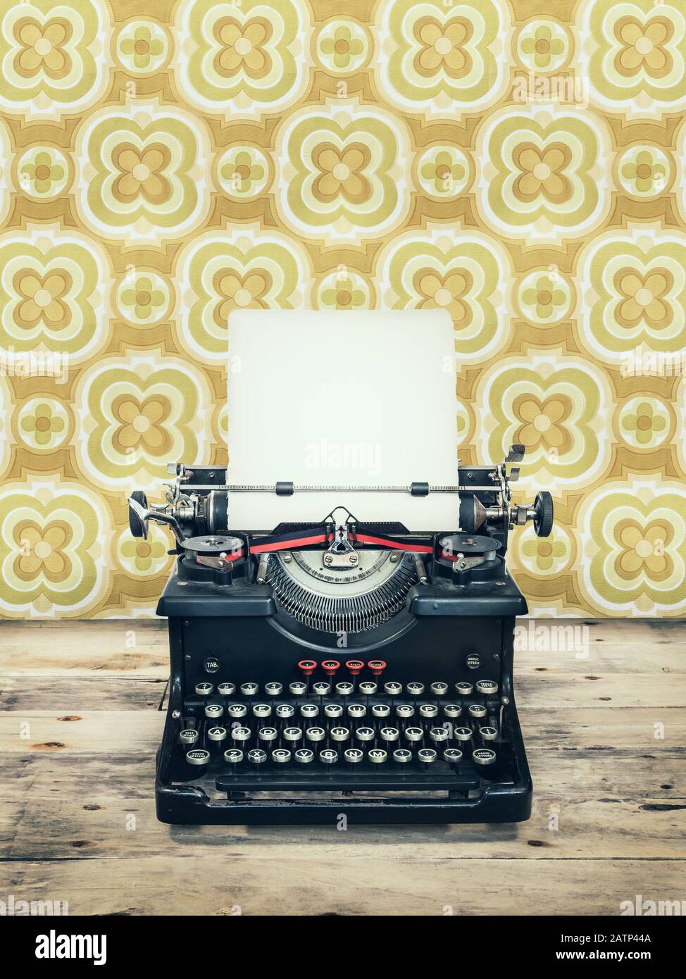 Retro-Motiv einer alten Schreibmaschine auf Holzboden mit Vintage-Tapete dahinter Stockfoto