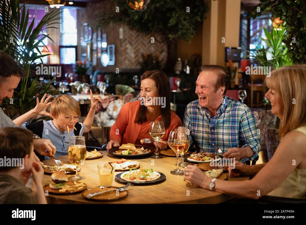 Eine Familie, die ein Essen in einem Restaurant hat. Ein kleiner Junge bringt sie alle zum Lachen, indem er ein Gesicht mit Essen macht. Stockfoto