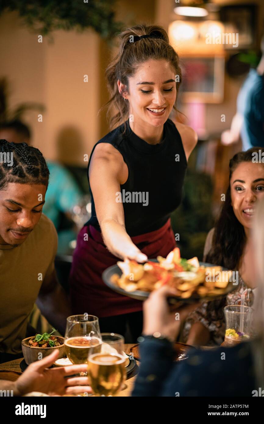 Eine Kellnerin, die Kunden in einem Restaurant eine Mahlzeit serviert. Stockfoto