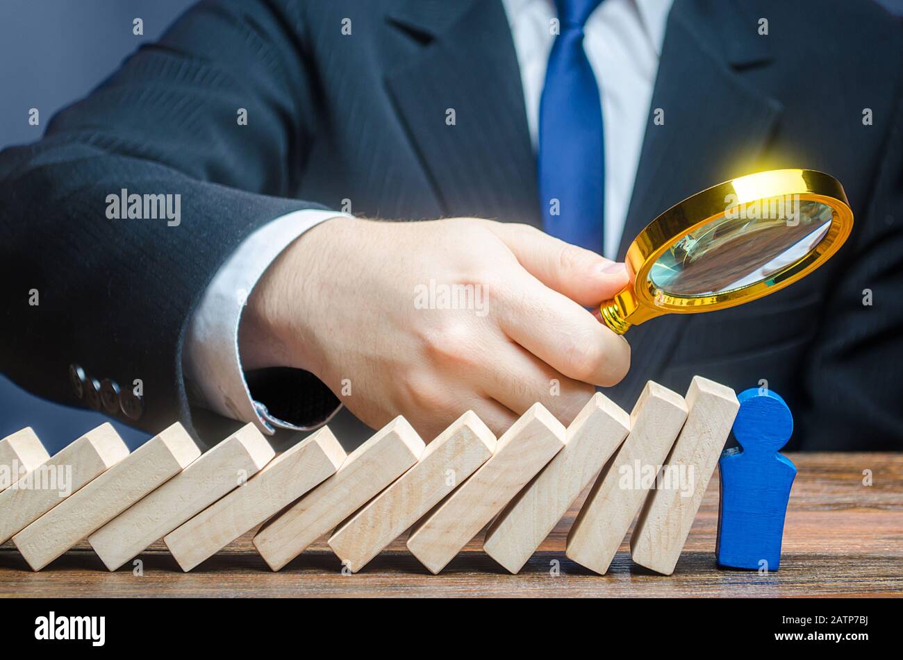 Ein Geschäftsmann untersucht den Stresswiderstand einer blauen Führerfigur nach einem Dominofall. Erledigen Sie Aufgaben, brillante Arbeitsleistung und Verantwortung Stockfoto