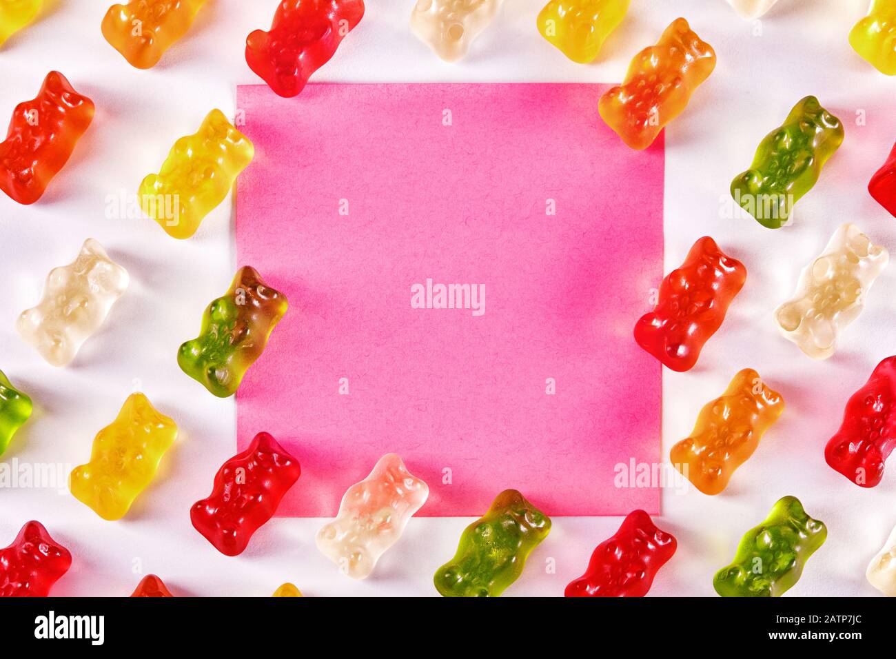 Flaches Laiendesign aus Gummibären-Bonbons mit einem rosafarbenen leeren Notizpapier. Stockfoto