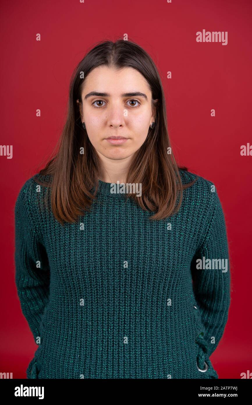 Vorderansicht des attraktiven brünetten Mädchens im Pullover isoliert auf rotem Hintergrund. Stockfoto