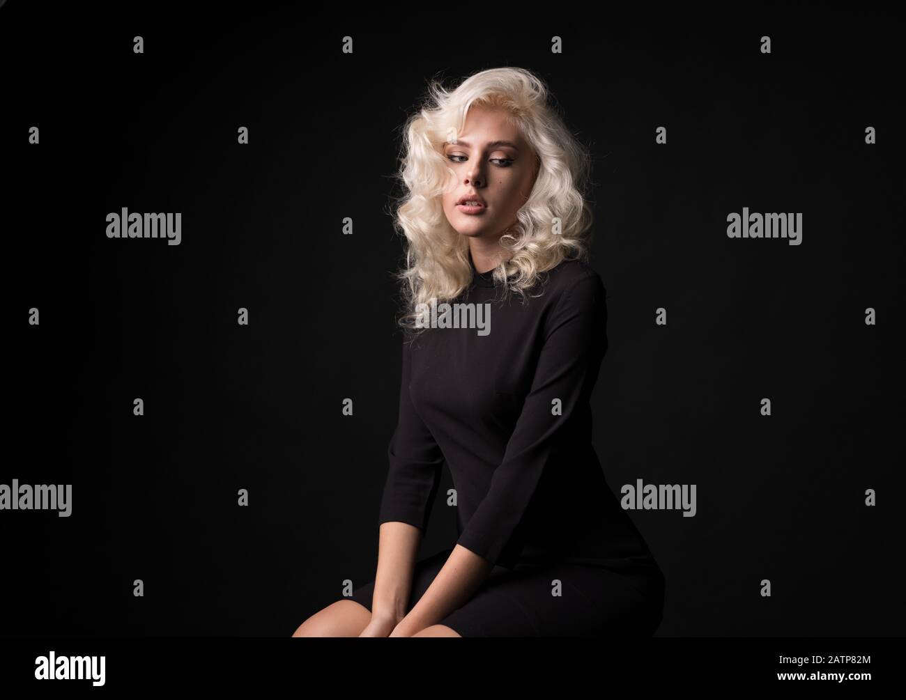 Schlankes blondes lockiges Mädchen, isoliert auf schwarzem Hintergrund. Stockfoto