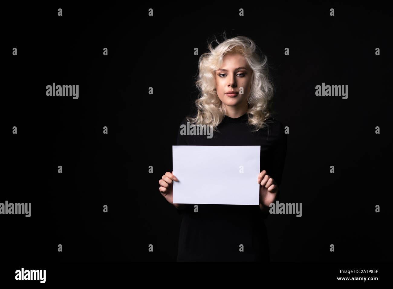 Vorderansicht des blonden Mädchens mit leerem Papier isoliert auf schwarzem Hintergrund. Stockfoto