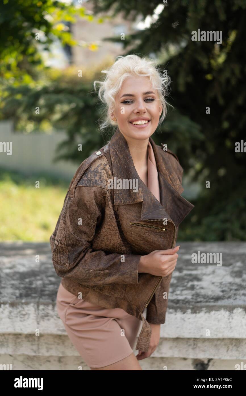 Fröhliches blondes Mädchen mit Lederjacke lächelnd auf der Straße. Stockfoto