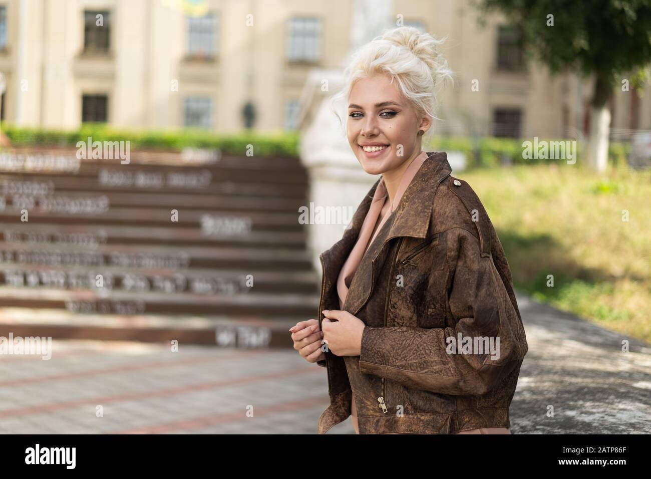 Fröhliche blonde Frau mit Vintage-Jacke lächelnd auf verwackelten Straßenhintergrund. Stockfoto