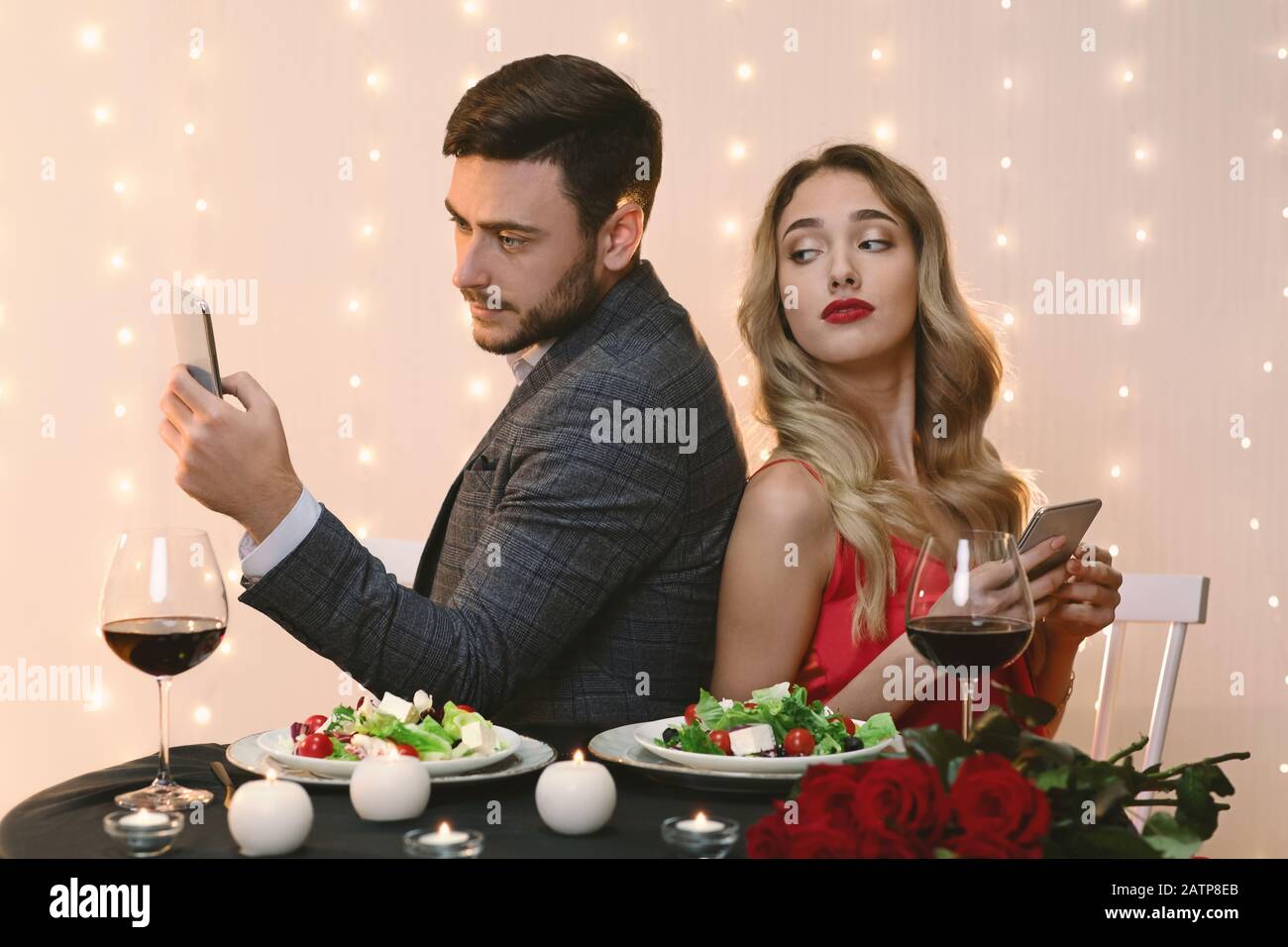 Neugierige Frau, die beim Romantischen Abendessen Im Restaurant Auf Das Smartphone Des Freundes feet Stockfoto