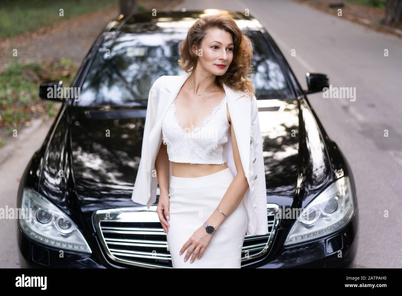 Schöne Frau in elegantem Outfit, in der Nähe des Autos stehend und wegblickend. Stockfoto