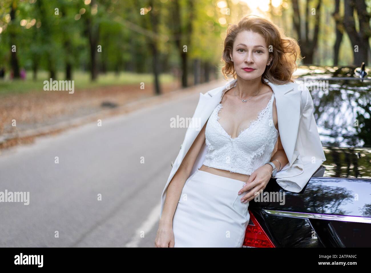 Elegante Frau in weißer Kleidung, die auf der Straße in der Nähe des Autos steht. Stockfoto