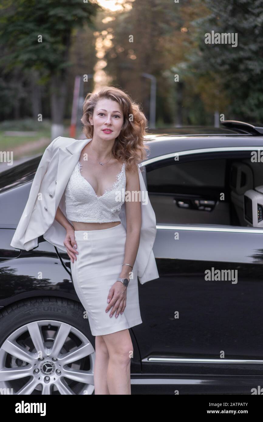 Gut aussehende Frau in weißer Kleidung, die in der Nähe des Autos steht. Stockfoto