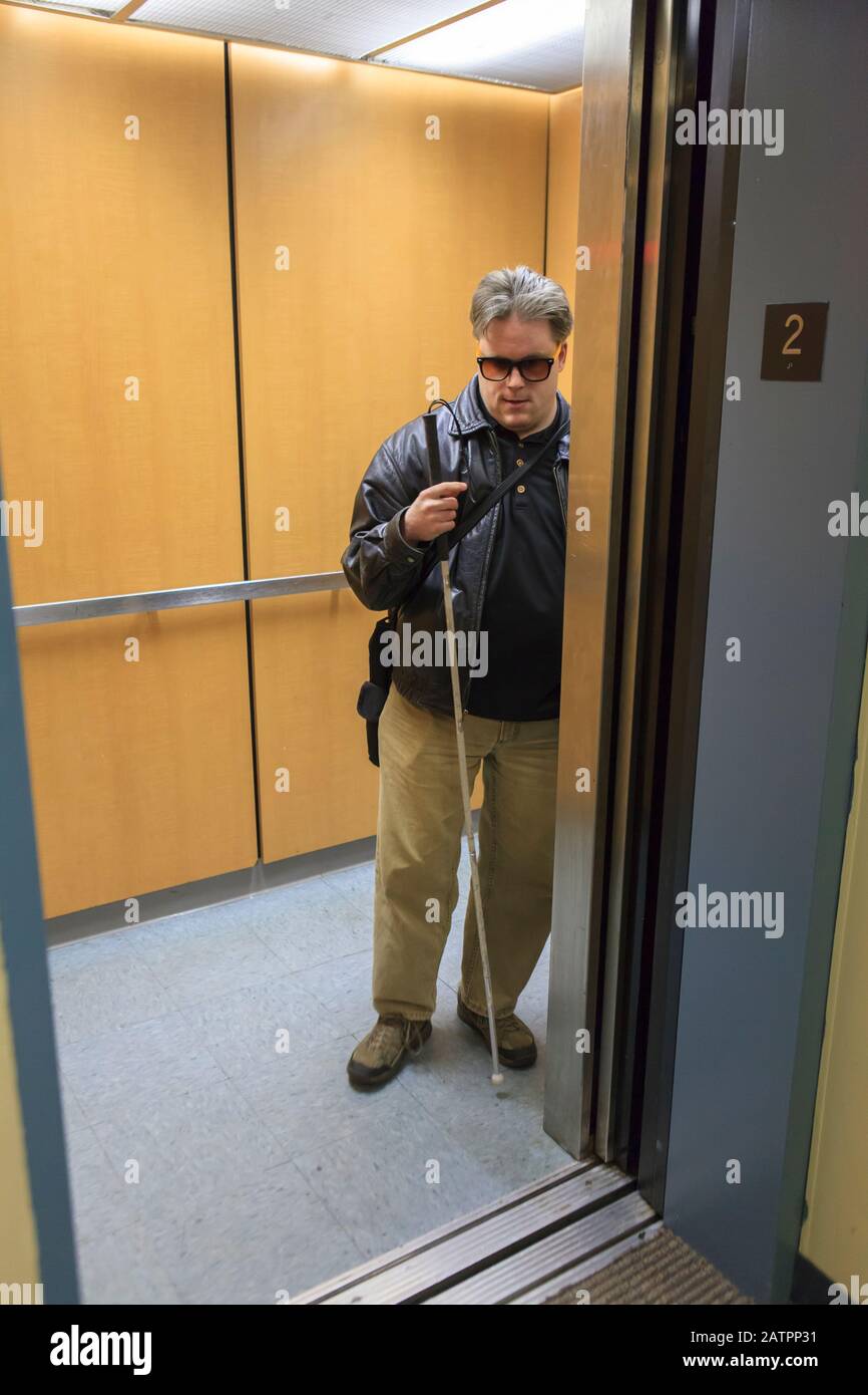 Mann mit Sehbehinderung steht in einem Aufzug mit Brille Und ein Spazierstock Stockfoto