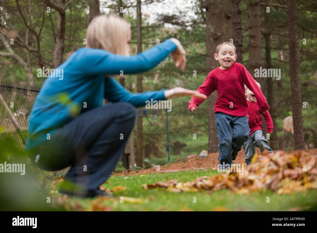 Mutter unterschreibt ihrem Sohn, in einen Haufen zu springen Von Blättern, wie er in einem Park auf sie zuläuft Stockfoto