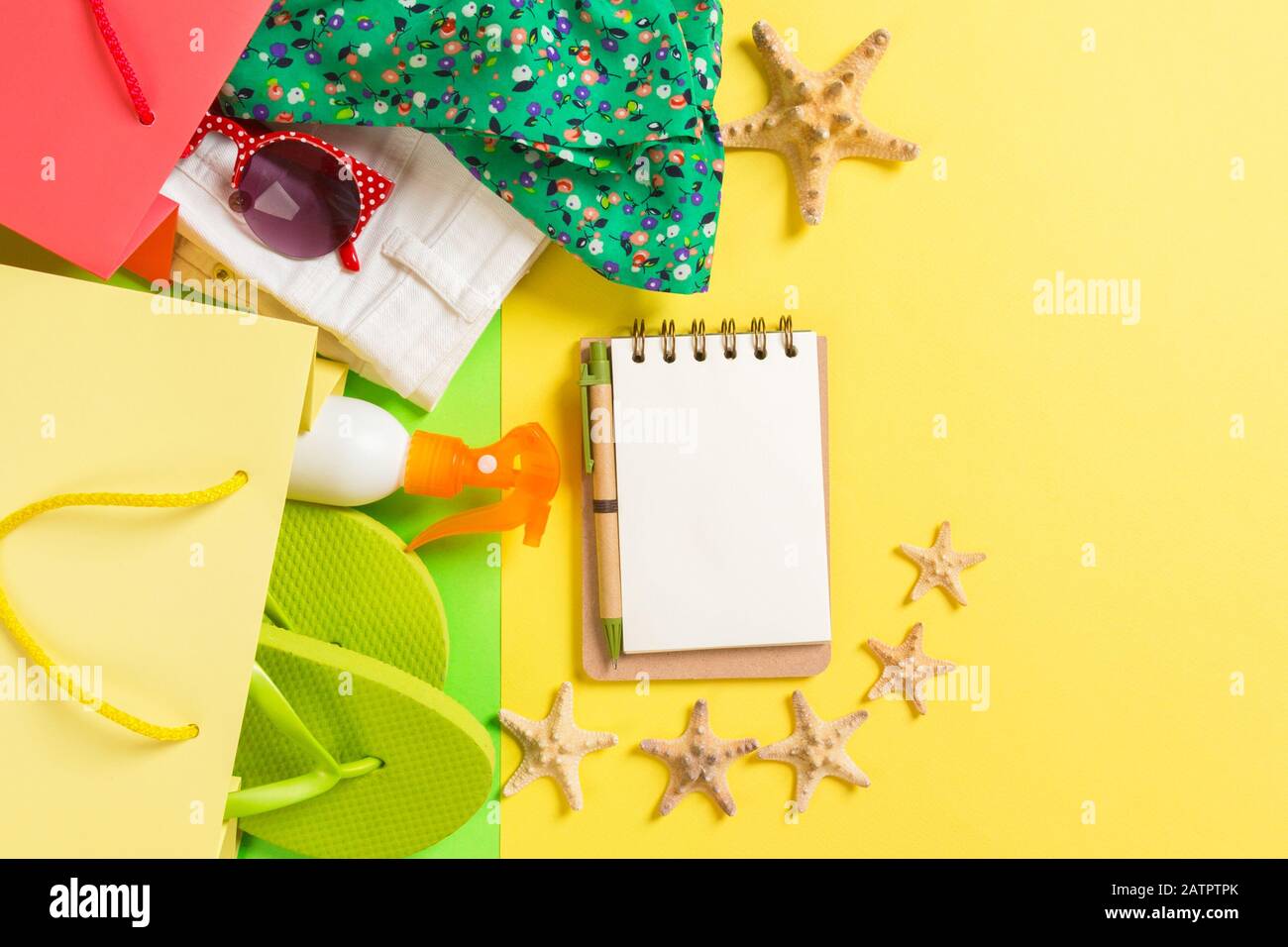 Sommer Konzept der bunten Tüten voller Kleider. Geschenkbeutel mit T-Shirt, denim Shorts, Flip Flops, Notebook und eine Flasche Sonnencreme. Sommer Stockfoto