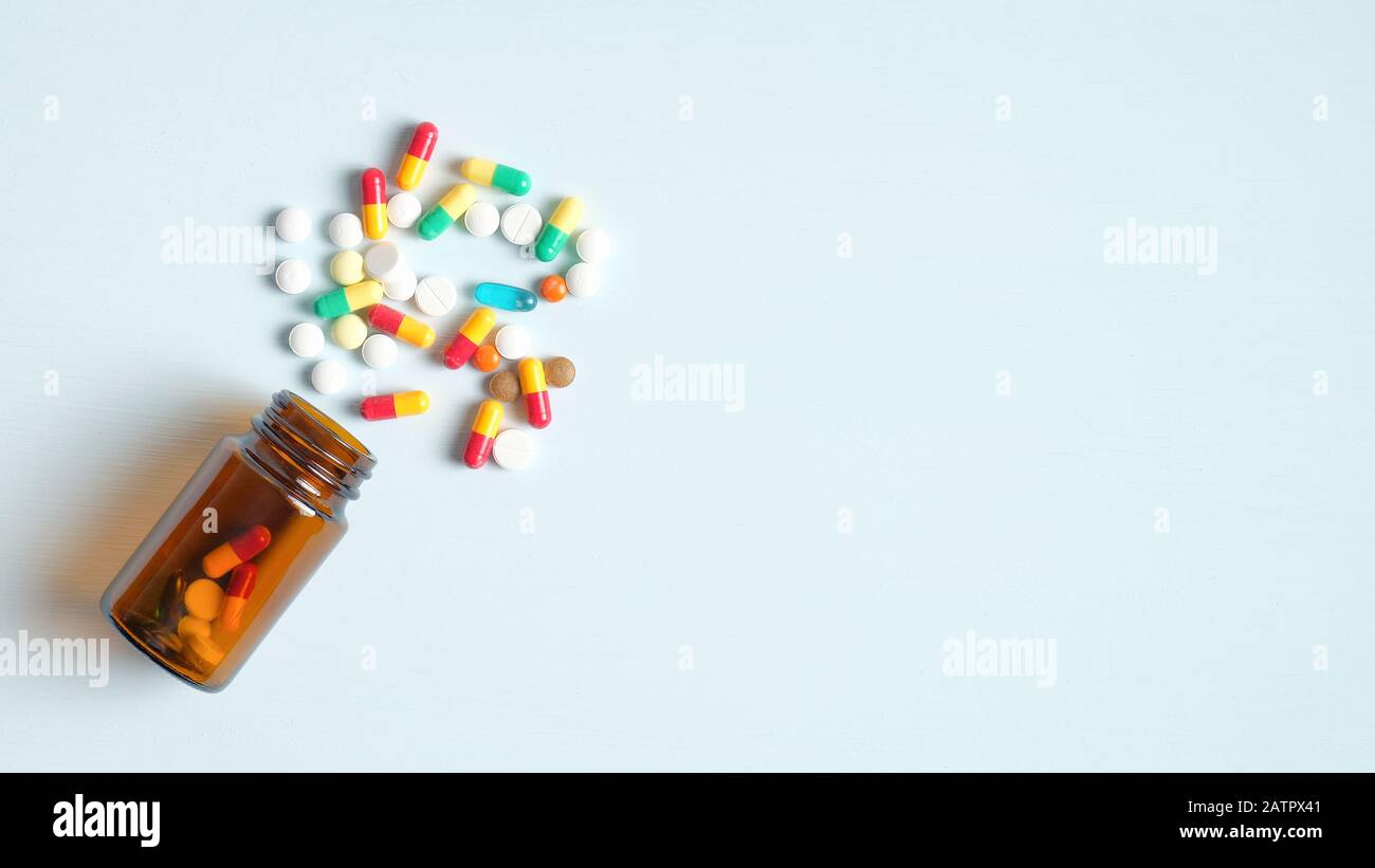 Mehrfarbige Pillen und braune Flasche auf blauem Hintergrund mit Kopierraum. Draufsicht. Konzept für das Gesundheitswesen, die Medizin und die Pharmazie Stockfoto