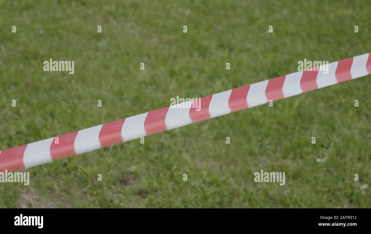 Rotes und weißes temporäres Umfassungsband auf dem Hintergrund von grünem Gras. Stockfoto