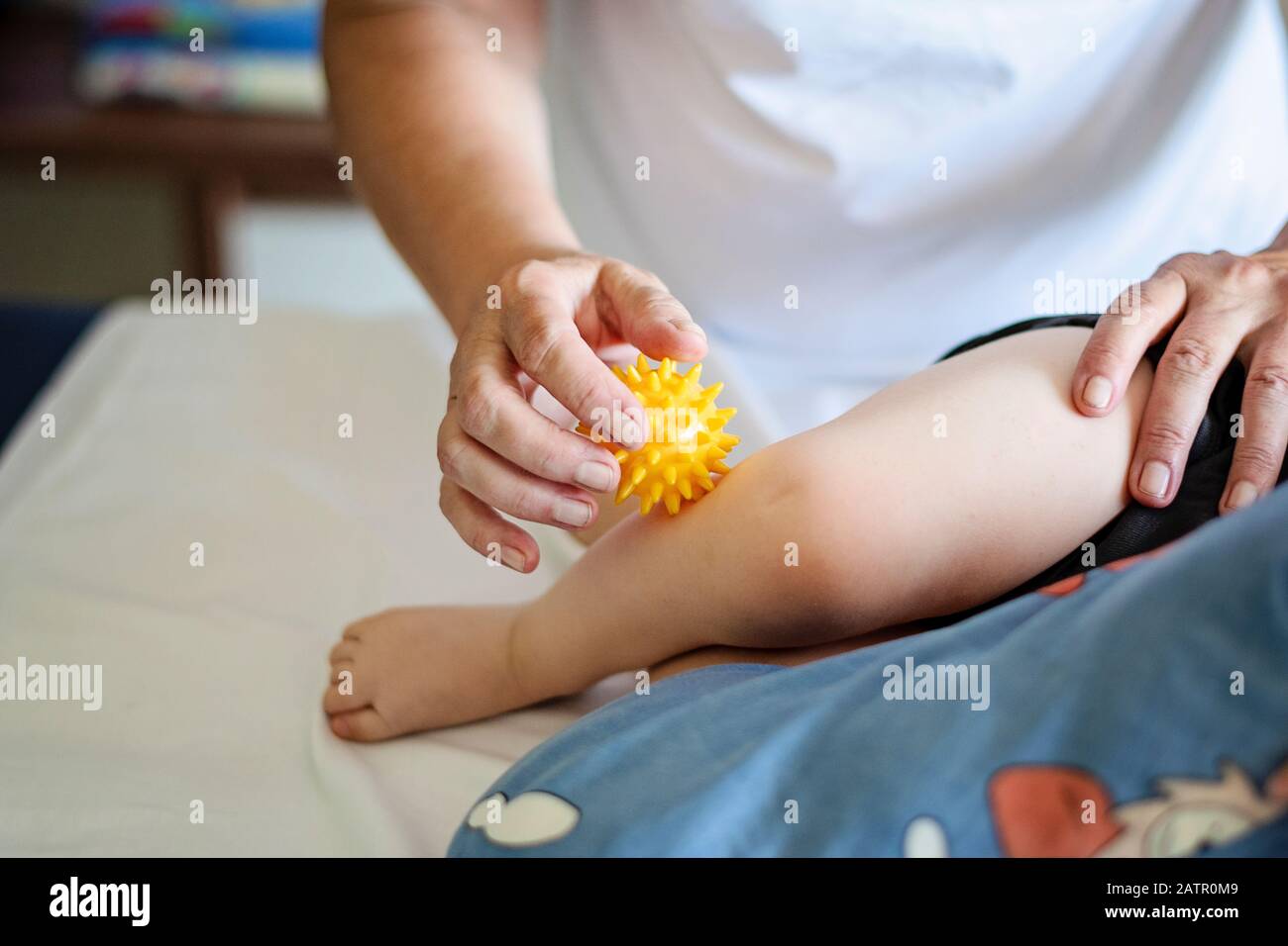 Baby mit Fußmassage in einem Rehabilitationszentrum. Kleines Kind in der Therapie. Massage-Therapeut massiert ein Baby mit gelbem Massageball. Stockfoto
