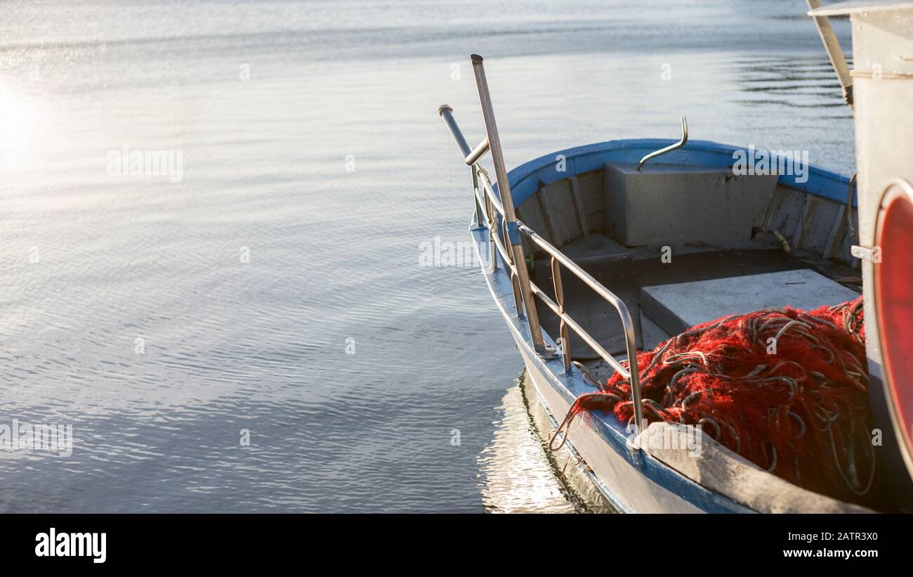 Ein festgelagertes Fischerboot wird vom Wasser geleult, während die Sonne am frühen Morgen mit der Winde des Fischerntnetzes im Vorland auf dem Meer reflektiert Stockfoto